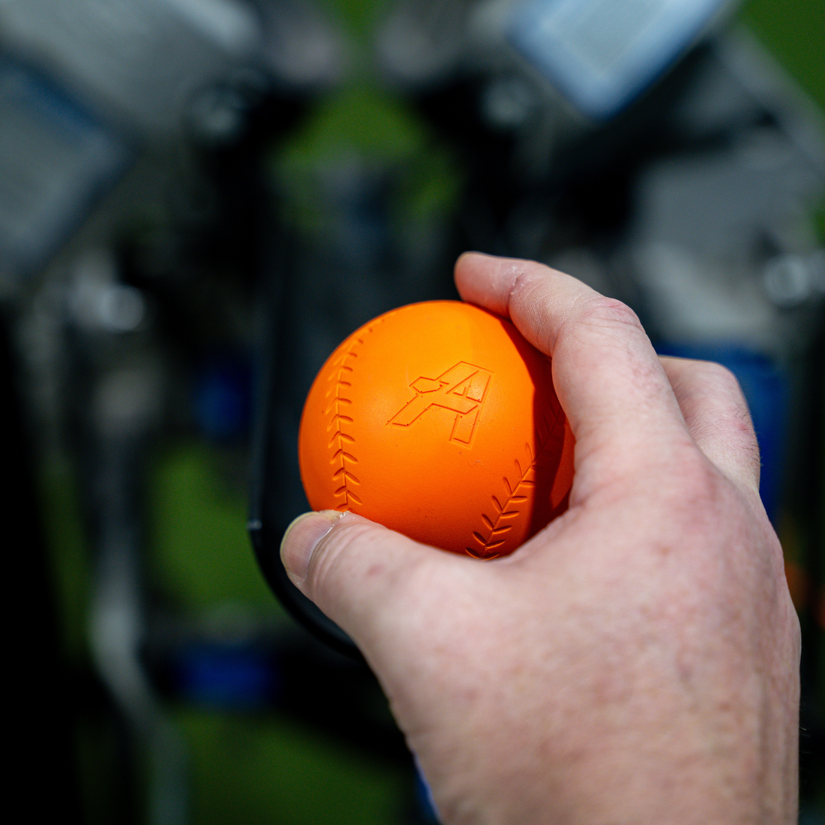 A close-up of a hand holding an orange Velomax, with a blurred outdoor background.