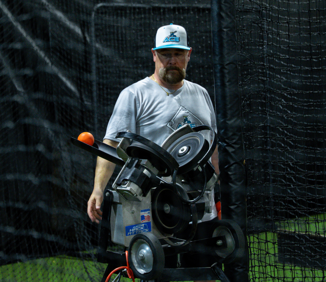 A coach feeding the Jr. Hack Attack in a batting cage